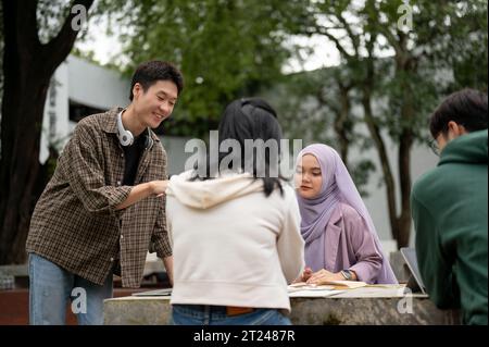 A cheerful and smart young Asian male college student is tutoring math to his friends in a campus park. Education concept Stock Photo
