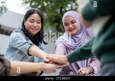 A group of cheerful, diverse Asian university students is putting their hands together, encouraging and supporting each other as a team. Friendship co Stock Photo