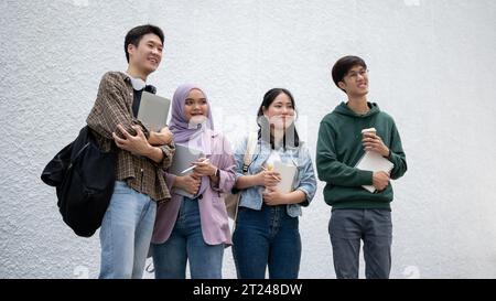 A group of happy, diverse young Asian college students in casual clothes are standing outdoors together. University life, friendship, education Stock Photo