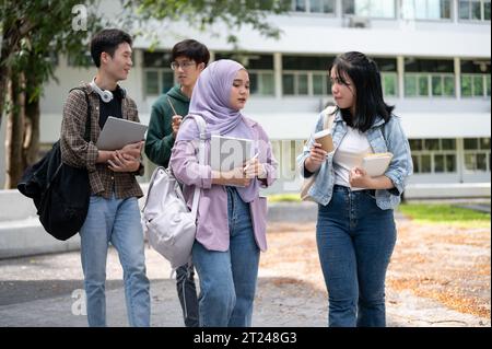 A group of diverse Asian university students are talking and sharing their ideas while walking down the footpath in the campus park together. Universi Stock Photo