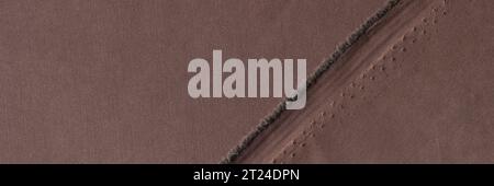 Straight undone seam of brown fabric by torn edge of cloth Stock Photo
