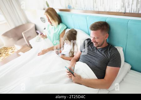 Close-up of family stare in smartphone, morning in bed with devices, kill time. People addicted to modern technologies, bored. Social media, addict co Stock Photo