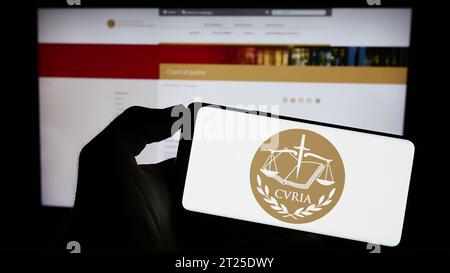 Person holding cellphone with logo of EU institution European Court of Justice (ECJ) in front of webpage. Focus on phone display. Stock Photo