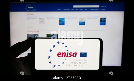 Person holding smartphone with logo of European Union Agency for Cybersecurity (ENISA) in front of website. Focus on phone display. Stock Photo
