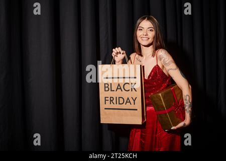 joyous lady with piercing and tattoos holding present and looking at camera, black friday concept Stock Photo
