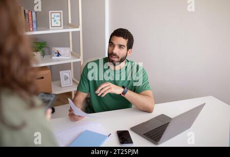 Calm millennial muslim man ceo with laptop talking to manager with documents Stock Photo