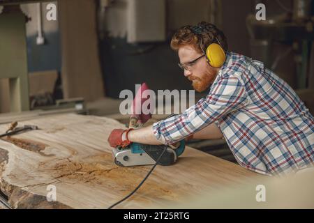 Bearded male wood worker using electric sander for wood. Carpentry workshop. High quality photo Stock Photo