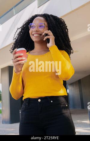Young smiling black woman at mobile phone while drinking coffee. Stock Photo
