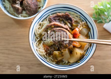 Beef noodle soup. Taiwanese famous food with sliced red braised beef and vegetables in a bowl on wooden table background. Stock Photo