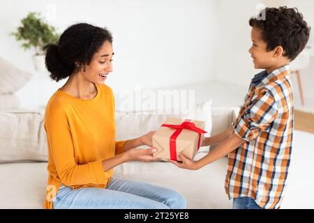 Son presents birthday present to mom indoors, cherishing special moments Stock Photo