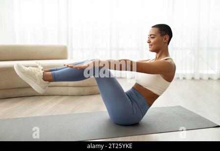 Cheerful young latin lady in sportswear doing exercises for abs on mat Stock Photo
