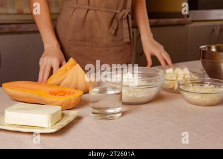 woman cook in kitchen apron in front of table with ingredients for making pumpkin pie at home Stock Photo