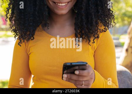 Closeup beautiful smiling black woman holding, using and looking at a smartphone Stock Photo