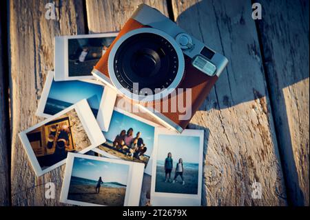 A vintage instant camera and several photographs lie on a wooden table. Stock Photo