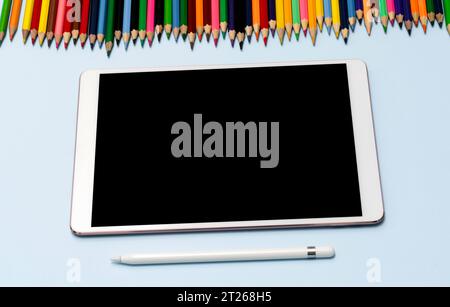 A tablet, stylus, and colored pencils lie on the table. View from the top. High quality photo. The concept of online education, training, private draw Stock Photo