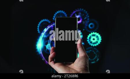 a hand holds a smartphone black screen, background a machine hologram. Stock Photo