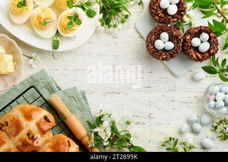 Easter brunch or breakfast. Easter chocolate nest cake with chocolate candy eggs, traditional hot cross buns and deviled eggs with bouquets of bloomin Stock Photo