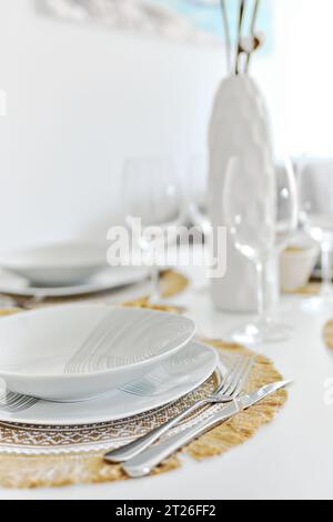 Close up white porcelain tableware plates on place mats and empty wine glasses ready for dinner. Table settings wait for guests at home or restaurant, Stock Photo