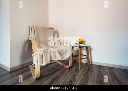 Red wooden modern armchair with opened book and yellow flowers on the small table near it. Decor, style Stock Photo