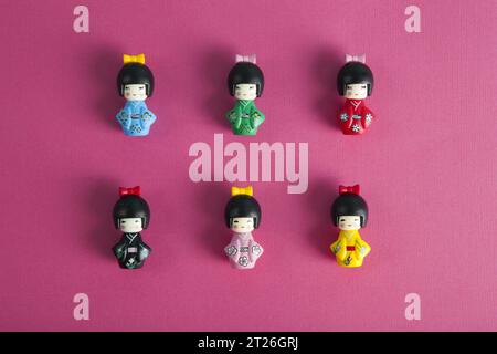 a collection of 6 wooden kokeshi dolls aligned in rows and columns on a fushia background. Minimalist, trendy still life photography. Stock Photo