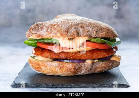 Bread roll with Nduja sausage, fresh tomato, onion, green lettuce, mayo, and some micro shoots. Stock Photo