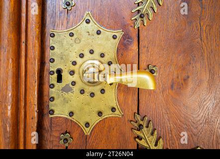 A metallic brass door handle on a wooden vintage door. Stock Photo