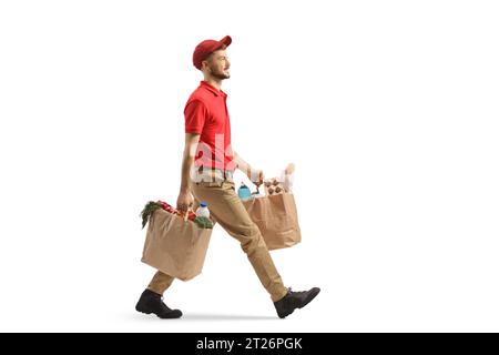 Full length profile shot of a delivery guy carrying bags with groceries and walking isolated on white background Stock Photo