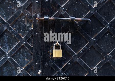 A padlock hangs on an old black metal door. Stock Photo