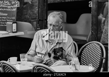 Local character smoking a pipe, sitting in a cafe with his dog in the old town of Antibes, France Stock Photo