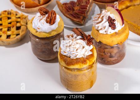 Traditional fall pies in small mason jars. Trendy portioned recipe of pumpkin, apple and pecan pie in small glass jars, with whipped cream toppings an Stock Photo