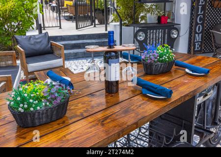 Close-up view of beautifully set wooden table at outdoor restaurant. In center, wine bottle with original holder for clean glasses. Miami Beach. Stock Photo
