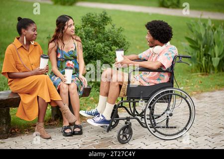 Black young man in wheelchair drinking coffee and telling story to his friends Stock Photo