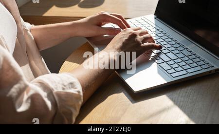 Female hands works at at laptop computer keyboard on wood table, desk, sunny day Stock Photo