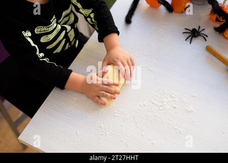 boy dressed as a skeleton kneading flour to make halloween cookies at home. Preparing halloween Stock Photo