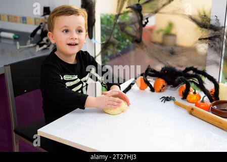 boy dressed as a skeleton kneading flour to make halloween cookies at home. Preparing halloween Stock Photo