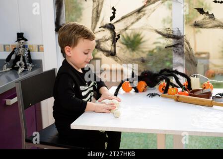 boy dressed as a skeleton kneading flour to make halloween cookies at home. Preparing halloween Stock Photo