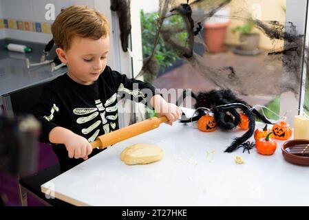 boy dressed as a skeleton kneading flour to make halloween cookies at home. Preparing halloween Stock Photo