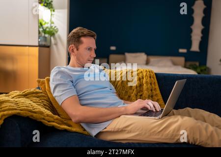 Serious man workaholic freelancer working on laptop in dark at home looking at screen. Stock Photo