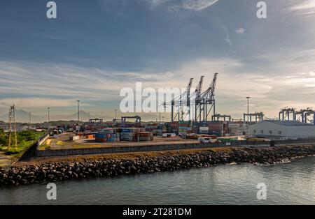 Guatemala, Puerto Quetzal - July 20, 2023: Morning light on container terminal in port with cranes, boxes and tall volcanos on horizon under blue clou Stock Photo