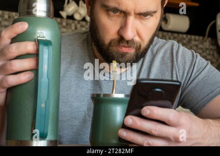 Young Caucasian Latino man drinking mate while checking his phone. Stock Photo