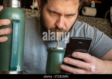 Young Caucasian Latino man drinking mate while checking his phone. Stock Photo