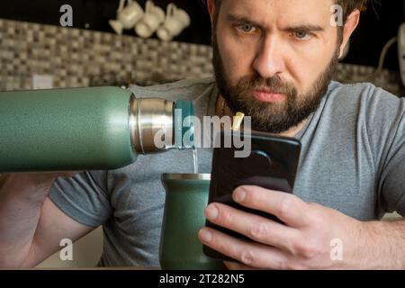 Young Caucasian Latino man drinking mate while checking his phone. Stock Photo