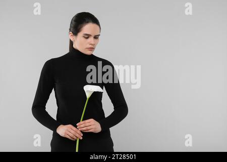 Sad woman with calla lily flower on light grey background, space for text. Funeral ceremony Stock Photo