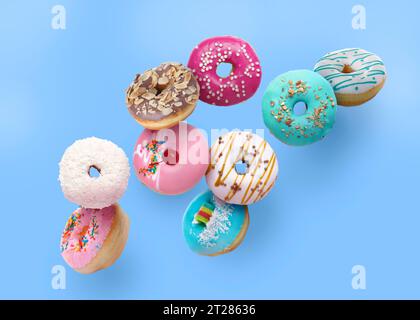 Different tasty donuts falling on light blue background Stock Photo