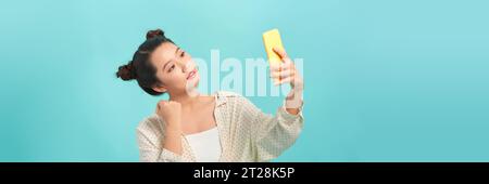 Cheerful Asian woman holding smartphone with fists clenched celebrating victory expressing success Stock Photo