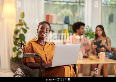 Portrait of happy Black woman with disability working on laptop in lounge area for students Stock Photo