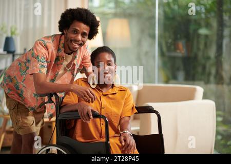 Portrait of smiling Black man and his girlfriend with disability spending time at home together Stock Photo
