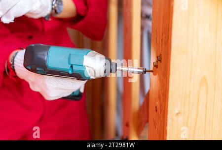 Carpenter and screwdriver hand tool. A skilled worker set to work drilling and installing wooden fixtures, using electric screwdriver to construct Stock Photo