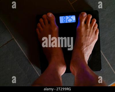 Men's feet on personal scale, body weight, measure, digital weight display in kilograms Stock Photo