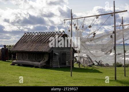 an old fishing net with buoys dries on poles and flutters in the wind against a background of a wooden house and the sea Stock Photo